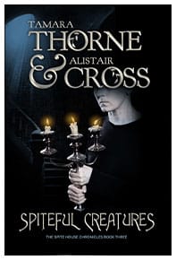 Book cover for Spiteful Creatures by Tamara Thorne & Alistair Cross: An older woman dressed in black holding a candelabra with three lit candles while standing at the bottom of a staircase.